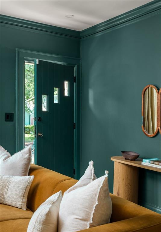 Living room with teal walls, an open front door, and a mustard sofa with white cushions.