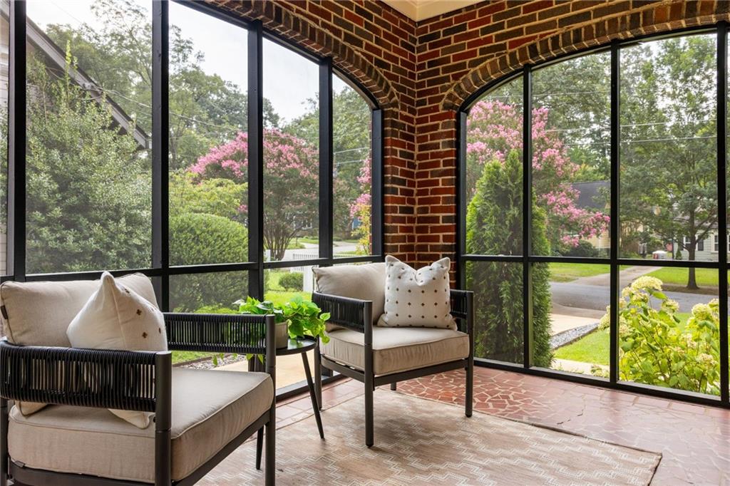 Furnished sunroom with arched brickwork, tall windows, and views of flowering trees.