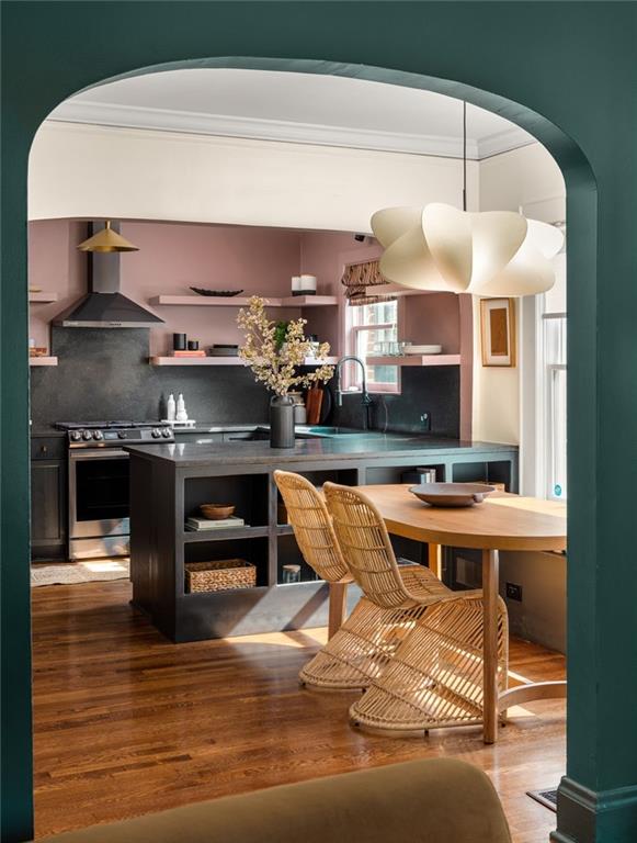 Kitchen with a dark stone island, pink walls, and a wooden dining table with rattan chairs.