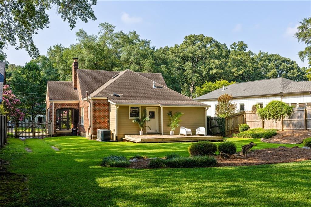 Rear of a brick-and-siding house with a raised deck and chairs overlooking a leafy backyard.