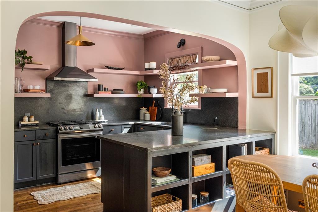 Kitchen with a pink arched alcove, dark cabinetry, stainless range, and large open-storage island.