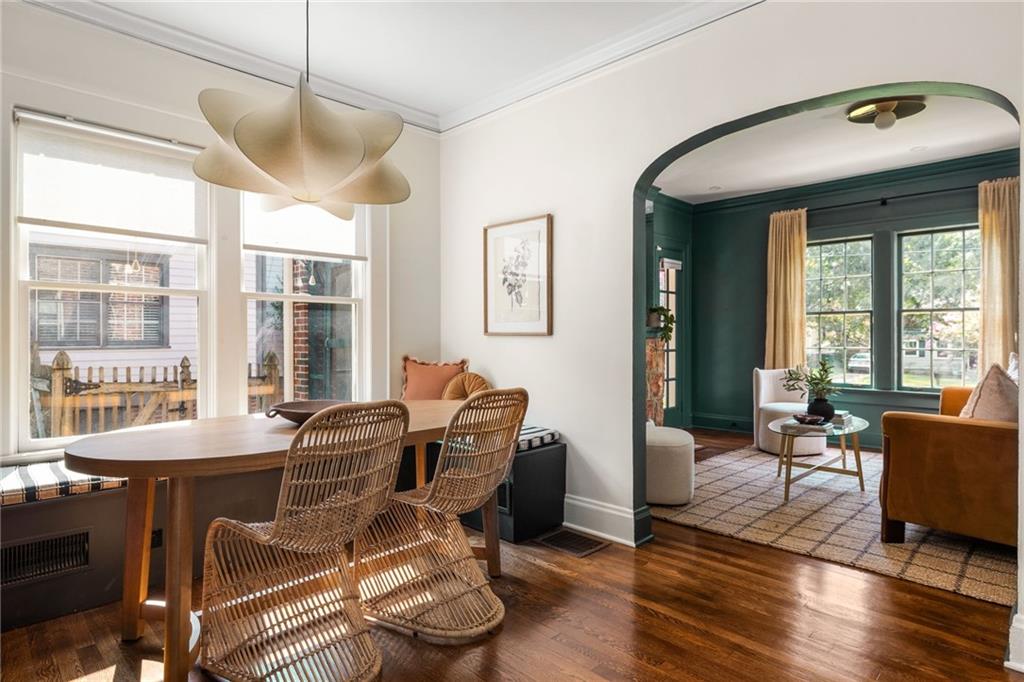 Dining room with a woven-chair table and window seat, opening into a dark green sitting room.