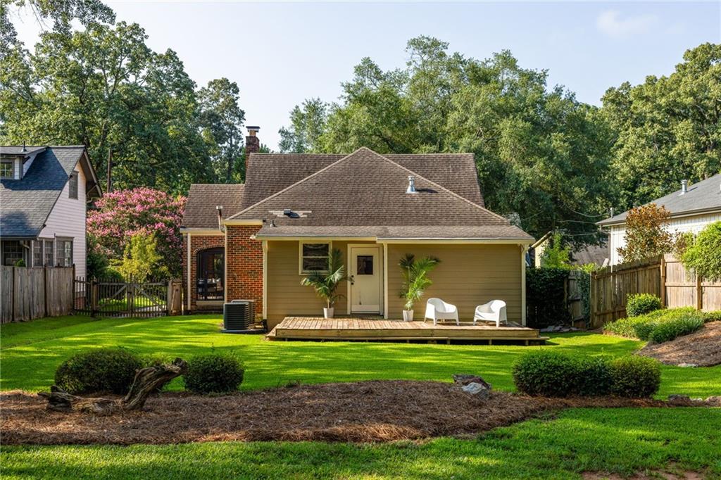 Home’s rear exterior with a small deck, two white chairs, and a green lawn.