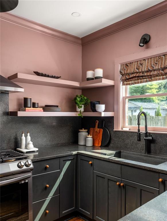 Kitchen with dusty pink walls, charcoal cabinets, open shelves, and a window above the sink.