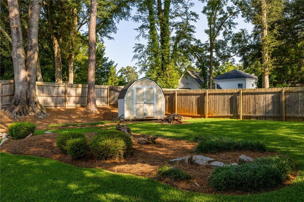 Backyard with a white storage shed, wooden privacy fence, mature trees, and landscaped lawn.