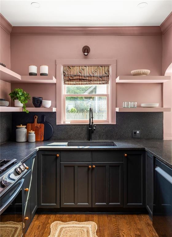 Kitchen with dark cabinets, charcoal counters, dusty pink walls, and a sink beneath a shaded window.