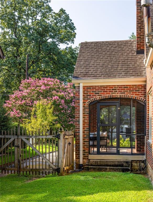 Brick house rear patio with a dark-framed glass door, wooden gate, and flowering trees.