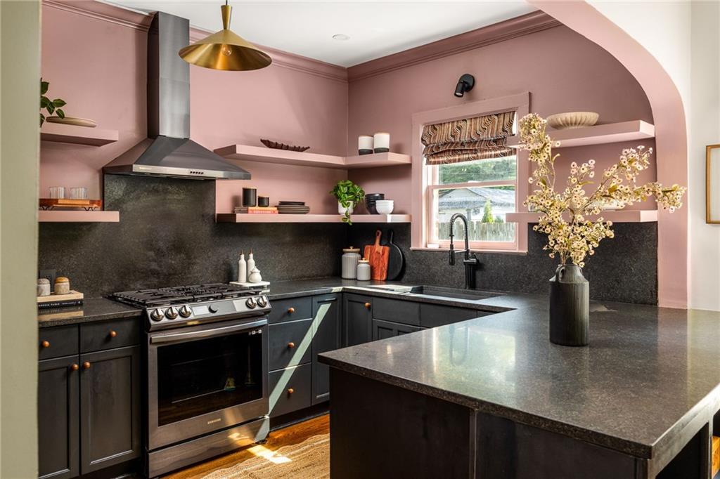 Kitchen with dusty pink walls, dark cabinetry, a stainless steel range, and a large stone island.