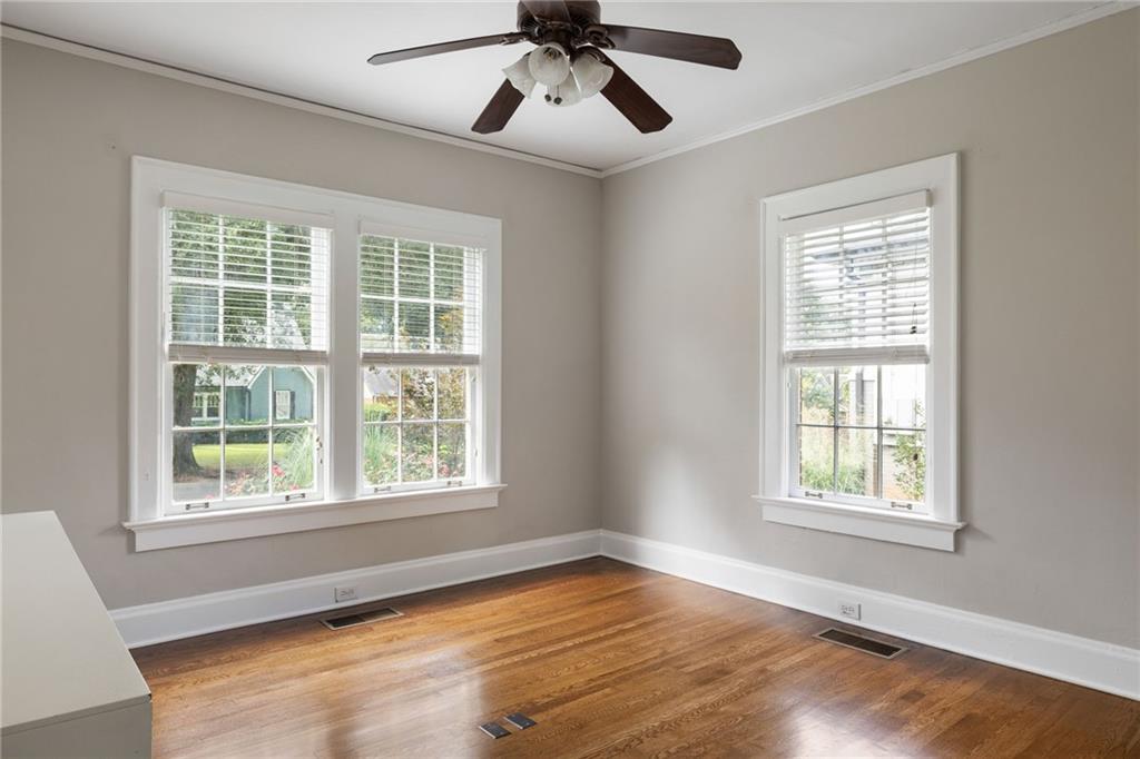 Empty room with hardwood floors, three windows, and a ceiling fan.