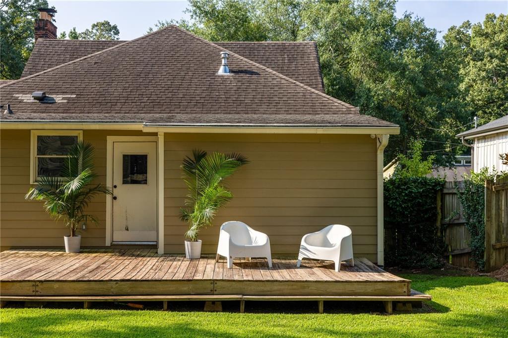 Rear of a tan house with a raised wooden deck, two white chairs, and potted palms.