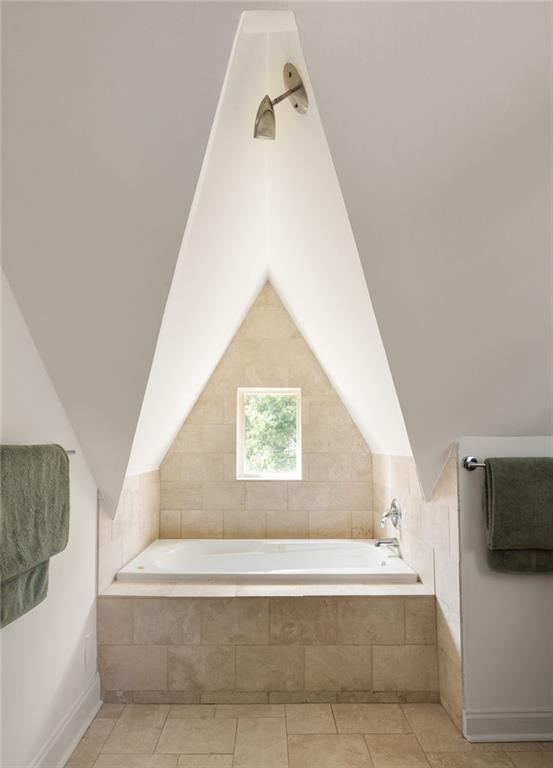 Bathroom with a built-in tub beneath a steep vaulted ceiling and small window.