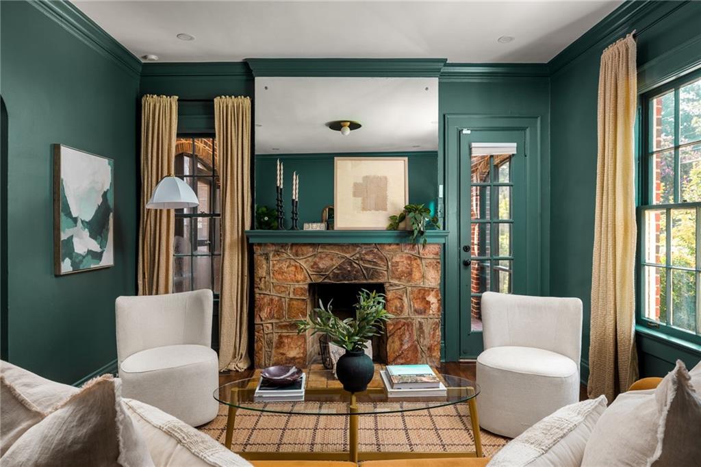 Living room with teal walls, a stone fireplace, cream armchairs, and gold curtains.