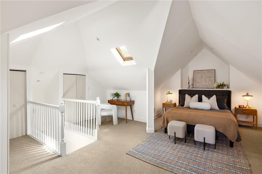 Upper-level bedroom with a bed beneath a vaulted ceiling and skylights.