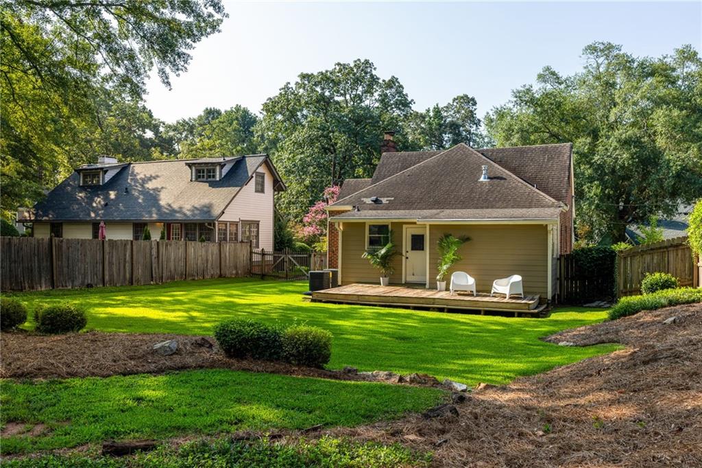 Rear of a house with a deck and white chairs overlooking a fenced green lawn.