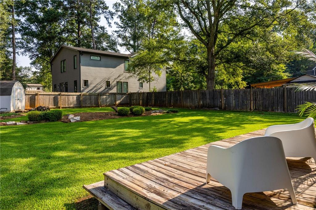 Fenced backyard with a broad lawn and raised wooden deck furnished with white patio chairs.