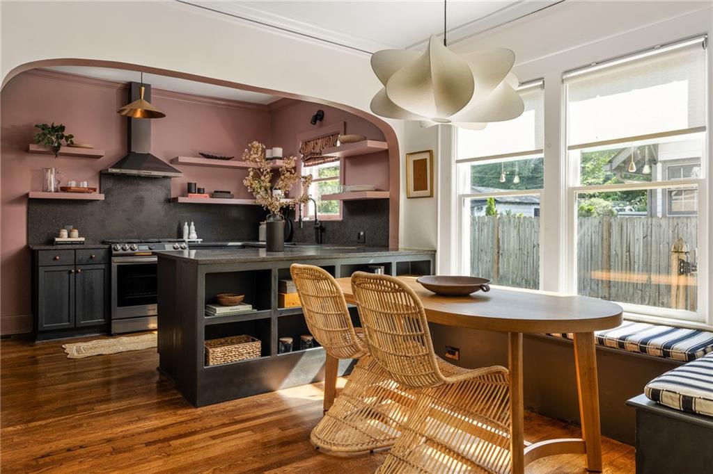 Kitchen and dining area with dusty rose walls, a dark island, woven chairs, and tall windows.