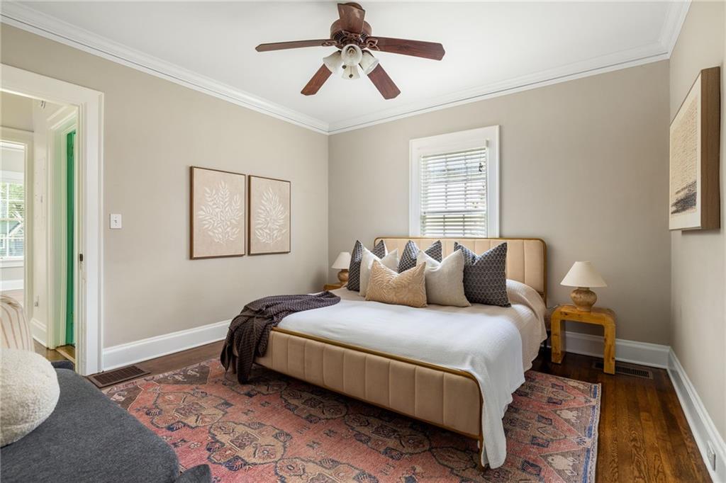 Staged bedroom with an upholstered bed, ceiling fan, hardwood floors, and patterned rug.