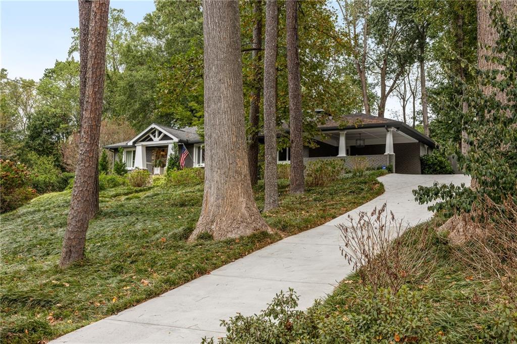 Single-story home among mature trees, with a sloped yard and curved driveway.