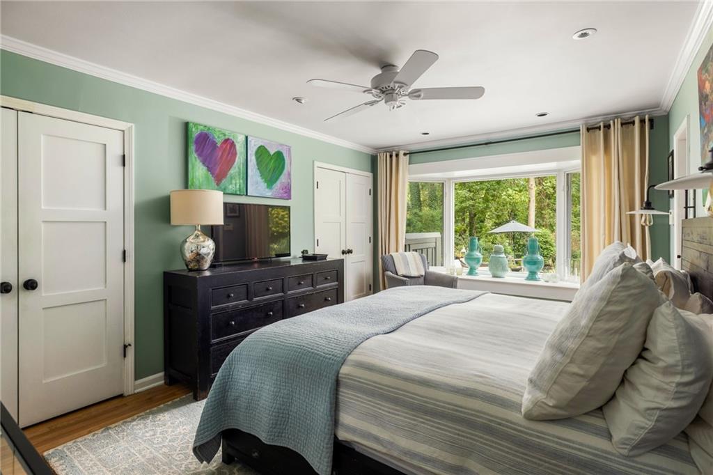 Furnished bedroom with a large bed, heart artwork, and a wide window overlooking greenery.