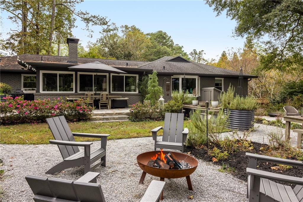Brick home with a gravel patio, Adirondack chairs, and a metal fire pit.