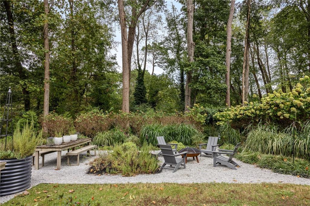 Gravel garden patio with Adirondack chairs around a fire bowl beneath mature trees.