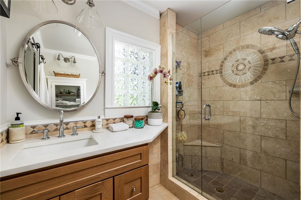 Bathroom with a stone-tiled glass shower, circular mosaic accent, and wood vanity beneath an oval mirror.
