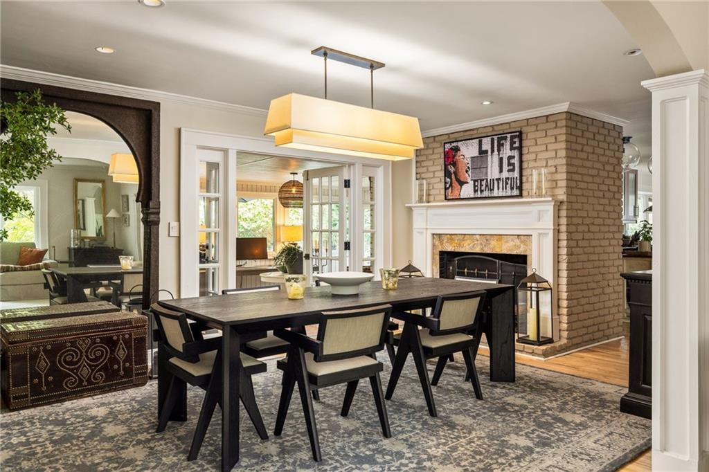 Dining room with a dark table, upholstered chairs, and a white fireplace against a brick wall.