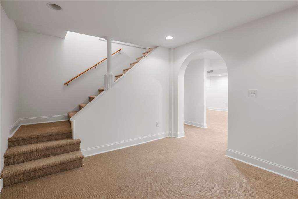 Empty carpeted room with a staircase and an arched doorway.