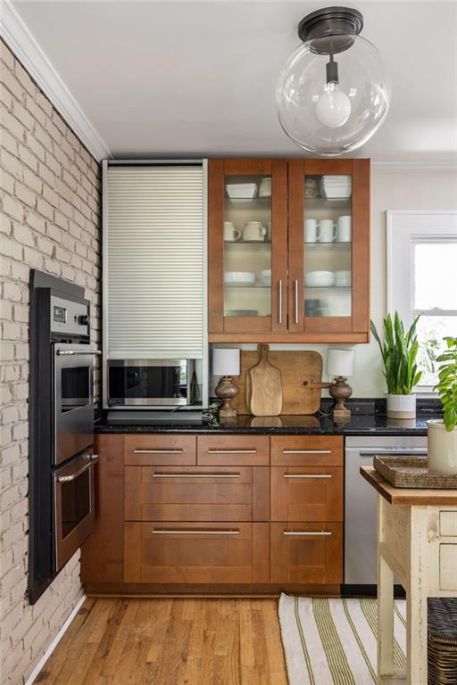 Kitchen with warm wood cabinets, black countertops, stainless steel appliances, and a white brick wall.