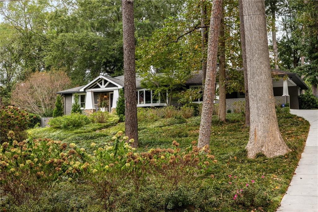Single-story brick home among mature trees, with a white front entrance and landscaped sloping yard.