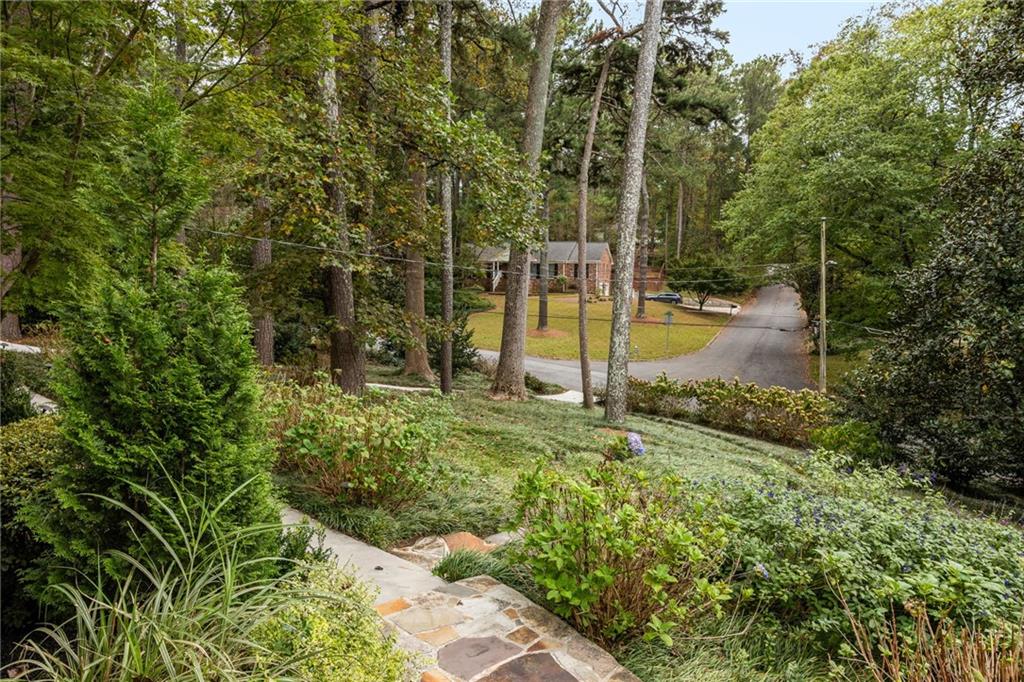 Landscaped front yard with a stone walkway winding through dense greenery beneath mature trees.