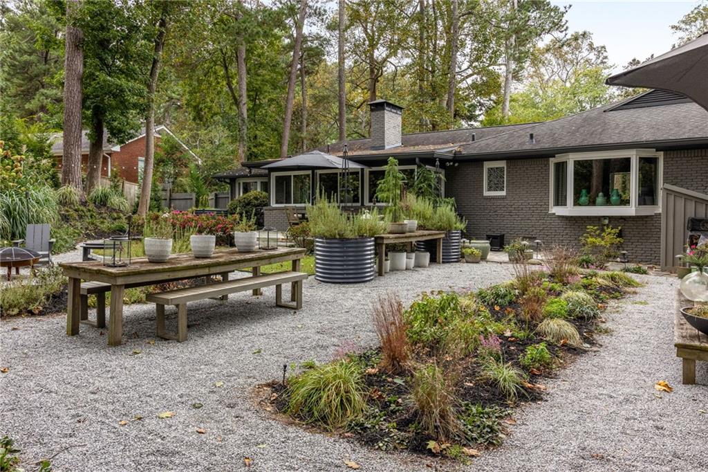 Gravel courtyard behind a brick house, with raised planters, garden beds, and a wooden picnic table.