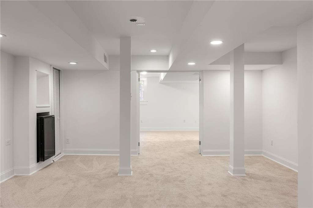 Carpeted room with two support columns, recessed lights, and a fireplace along the left wall.