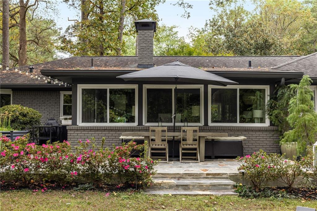 Brick home with a stone patio, outdoor dining set, and umbrella amid flowering shrubs.