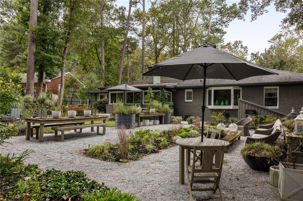Backyard patio with gravel seating area, large umbrellas, raised planters, and a single-story brick house.