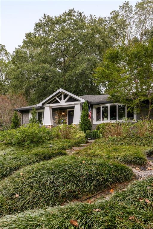 Single-story house with a covered entry above a sloped garden and mature trees.