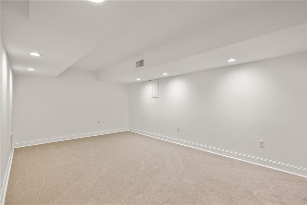 Empty finished basement room with beige carpet and recessed ceiling lights.