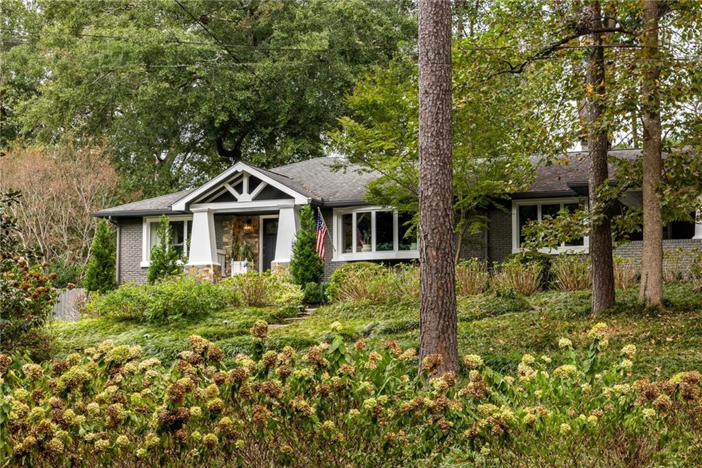 Gray-brick home with a white gabled entry, American flag, and wooded landscaping.