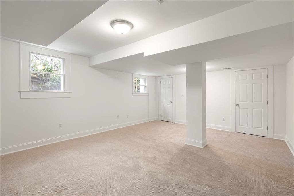 Empty carpeted basement room with a central support column and two windows.