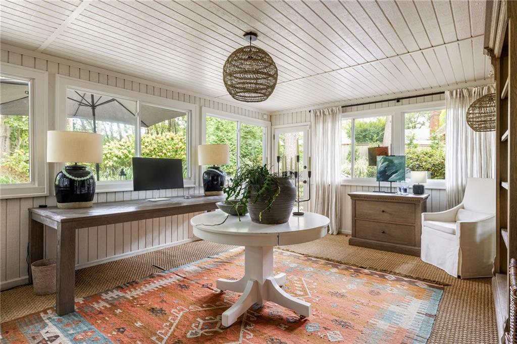Furnished sunroom with expansive windows, a long desk, and a colorful patterned rug.