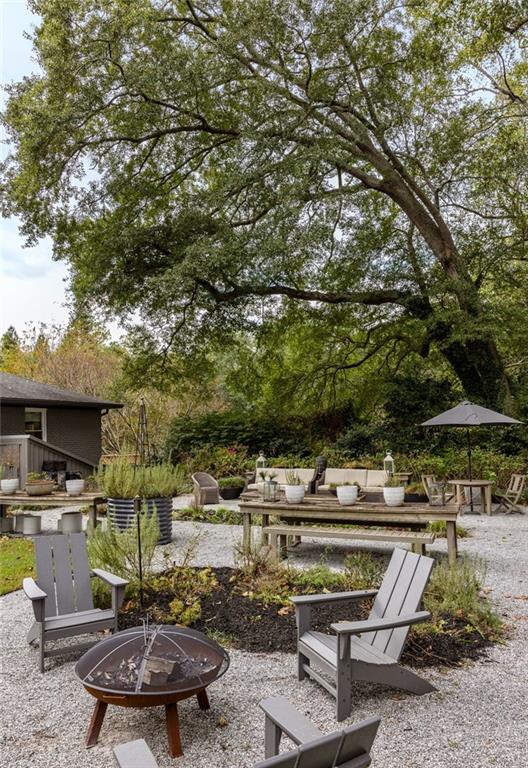 Gravel patio with Adirondack chairs and a fire pit beneath a large shade tree.