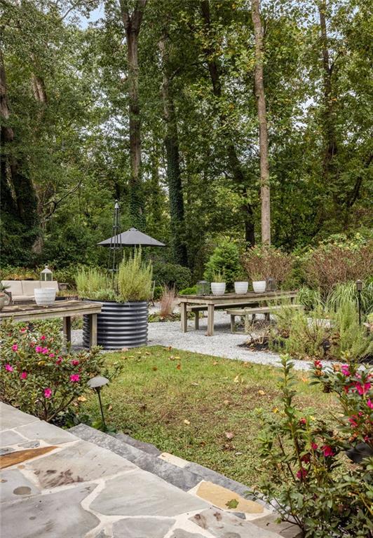Backyard garden with a stone patio, raised planter beds, flowering plants, and mature trees.