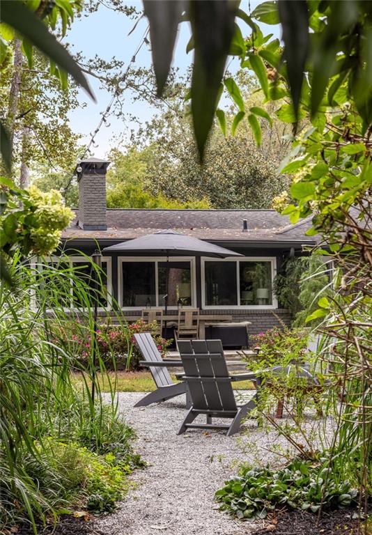 Brick home's garden patio with a gravel path, dark chairs, umbrella, and leafy landscaping.