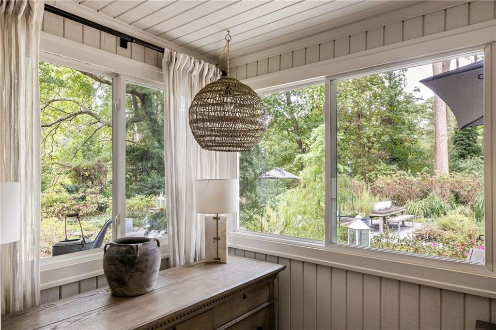 Sunroom with large garden-facing windows, white curtains, and a wooden console table.