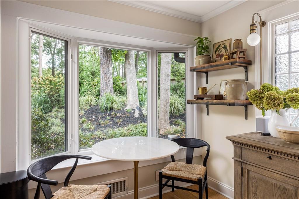 Breakfast nook with a round white table, black chairs, and large windows overlooking a leafy garden.