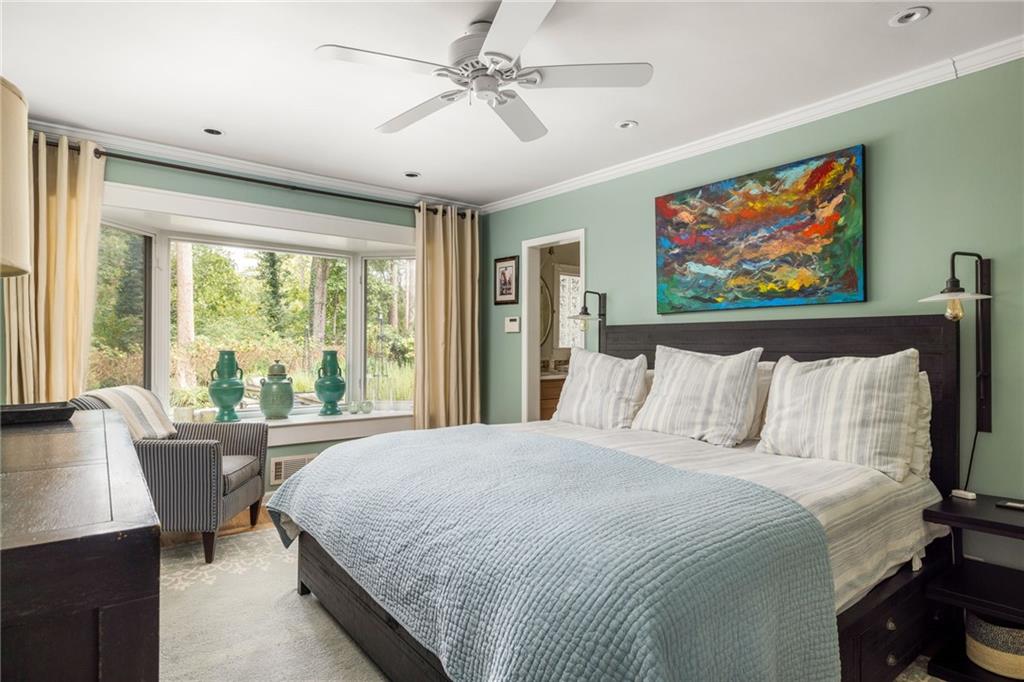 Bedroom with pale blue bedding, colorful abstract art, and a large window overlooking trees.