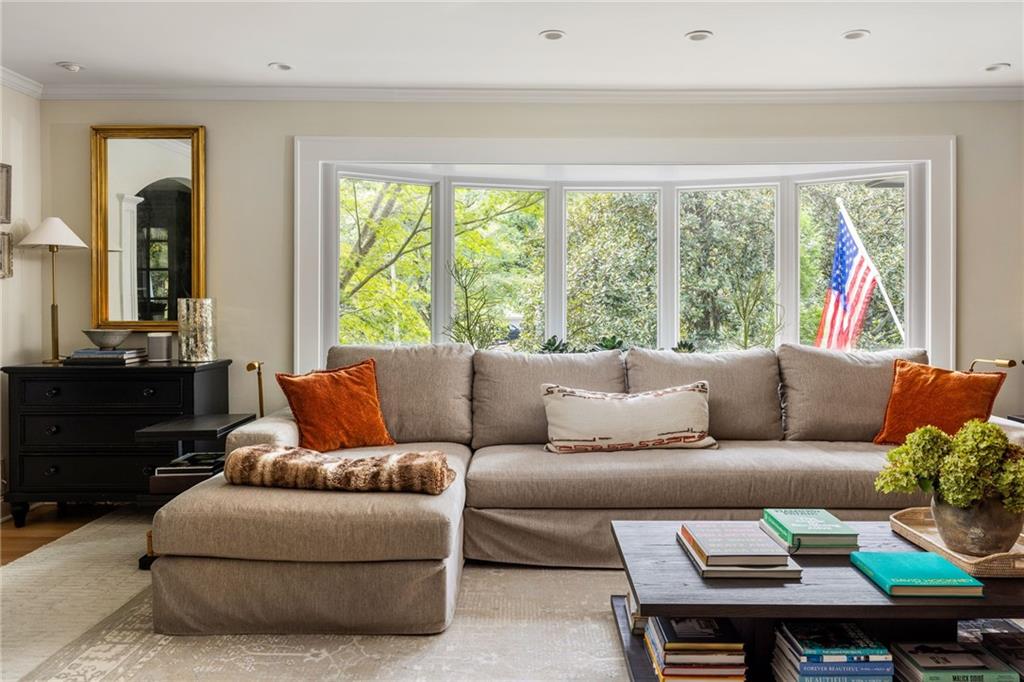 Living room with a gray sectional, rust-colored pillows, and a wide bay window overlooking trees.