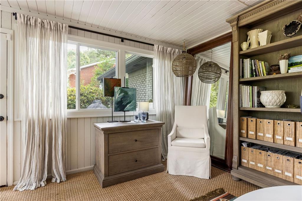 Furnished home office with a wood desk, wide windows, white chair, and built-in bookcase.