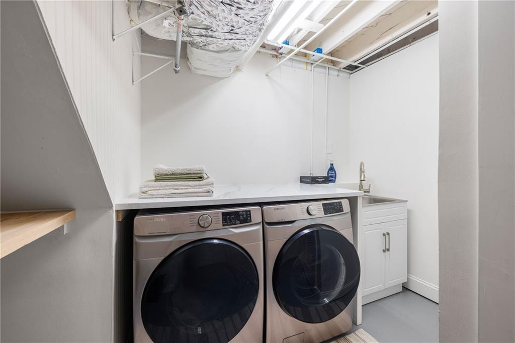 Laundry room with front-loading washer and dryer beneath a countertop beside a utility sink.