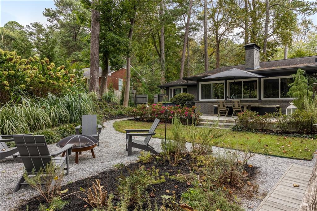 Home’s wooded backyard with a covered patio, gravel seating area, Adirondack chairs, and fire pit.